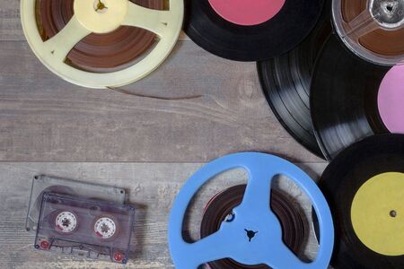 Old vinyl records, audio tapes and reels of magnetic tape on the tableの写真素材