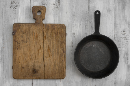 Old cast iron pan and cutting board are on the painted white tableの写真素材