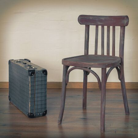 Old chair and an old suitcase stand in the background of a concrete wallの写真素材