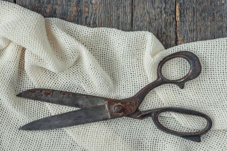 Old tailor scissors lying on white textured fabricの写真素材