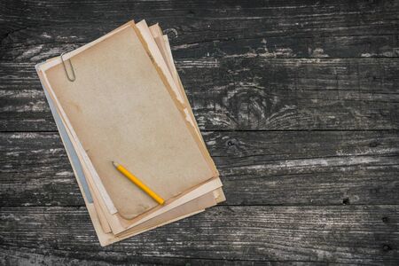 A stack of old paper and yellow pencil lying on a wooden tableの写真素材