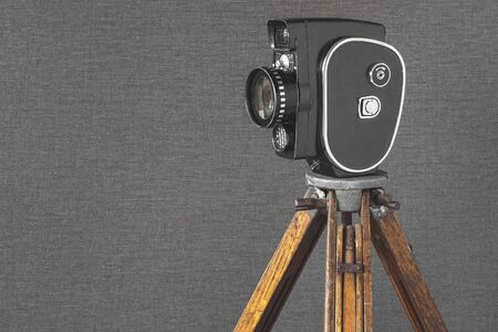 The old camera on a wooden tripod stands on a background of a wallの写真素材