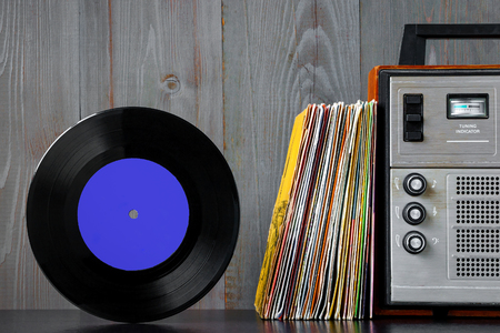A pile of old vinyl records and audio equipment stand on a shelf against the background of a wooden wallの写真素材