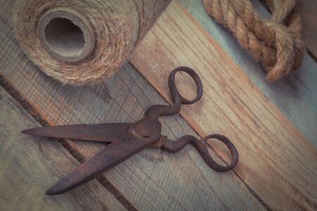 Old rusty metal scissors, a coil with a twine and a linen rope lie on a wooden tableの写真素材