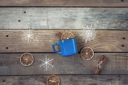 On a wooden table is a cup with a warming drink, cinnamon sticks, dried lemon and white snowflakes. A view from above.の写真素材