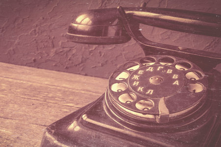 A fragment of a vintage telephone with a round dial set is shot close-up. A toned stylized photo.