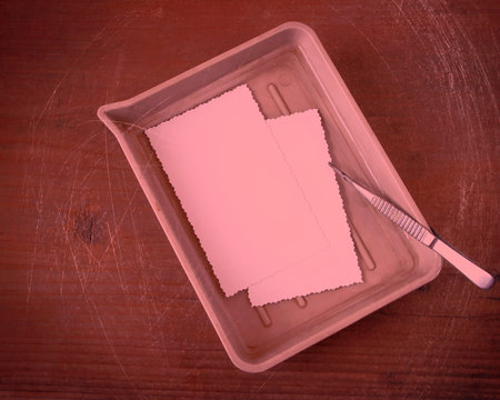 Cuvette with developer and metal tweezers for processing analogue photography is on the table in the...