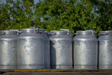 Cans for collecting milk stand against the apple gardenの写真素材