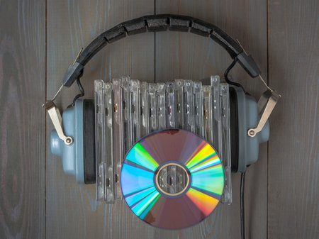 A stack of CDs and old audio headphones lie on a wooden table.