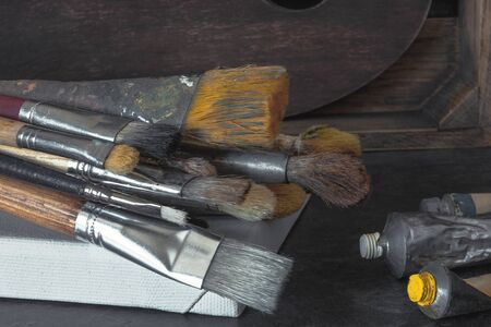 Working brushes of the artist, tubes of paint and canvas on a stretcher are on the table in the workshop. Art equipment.の写真素材