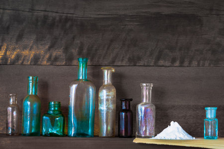 Old pharmacy bottles stand on a wooden shelf near a slide with white medicinal powder