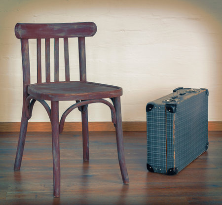 An old chair and an old suitcase stand in an empty room against a concrete wallの写真素材