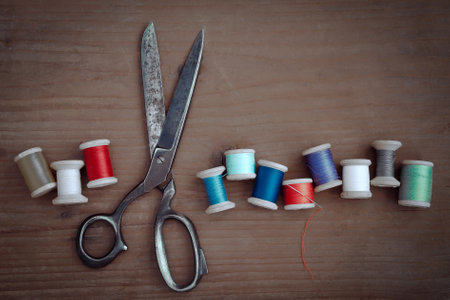 Old scissors and wooden spools of colored thread lie on a wooden tableの写真素材