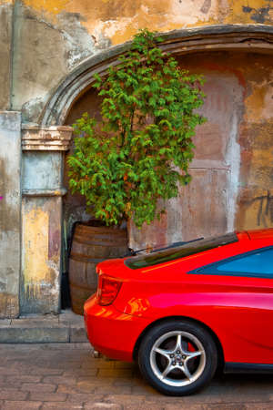 A fragment of a red sports car is shot against the background of a wall in the old townの写真素材