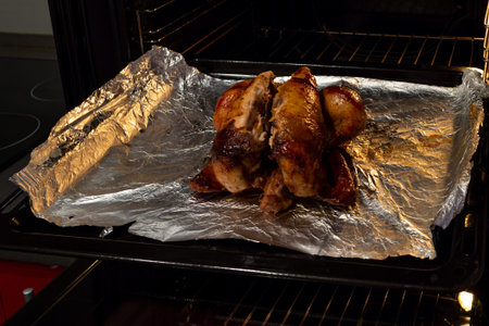 Delicious roasted chicken in the oven. In the background kitchen table and stove.