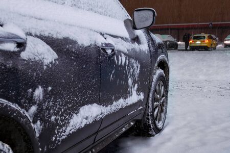 The car is covered with layers of snow and ice. Side view on doors and wheels. Close-up. Taxi driver removes snow from a car in the background. It's snowing, a blizzard. Winter nightの写真素材