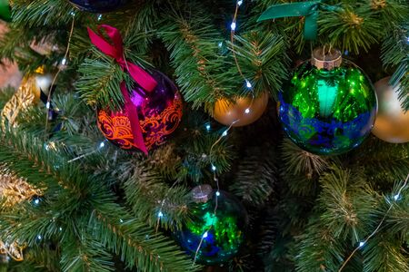 Christmas toys, balls of gold, purple and green colors, a shining garland hanging on the branch of the Xmas tree. Close-up.の写真素材