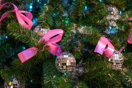 Christmas toys in the form of disco balls. and pink bows hanging on the branch of the Xmas tree. Close-up.の写真素材