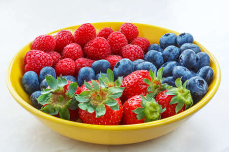 small fruits raspberries strawberries and blueberries closeup in a yellow plate, berry dessertの写真素材