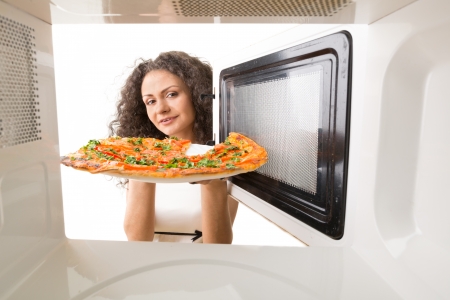 The girl gets a pizza out of the microwaveの写真素材