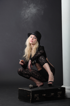 The girl smokes a cigarette while sitting on a suitcaseの写真素材