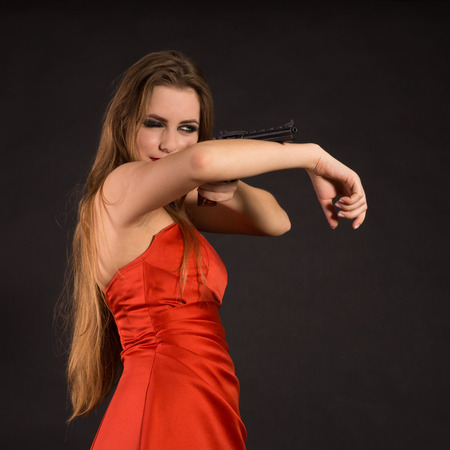 Green-eyed lady in a red dress with a gunの写真素材