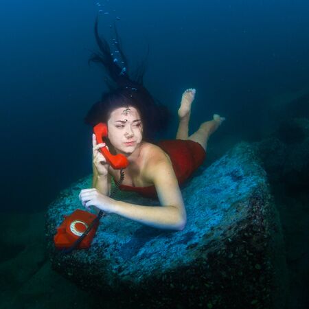 The girl lies on the bottom of the lake and chatting on the phoneの写真素材