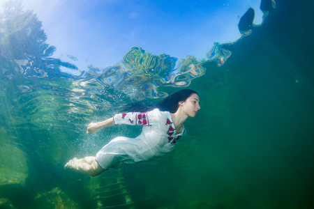 Young graceful woman dressed in a Ukrainian embroidery posing underwaterの写真素材