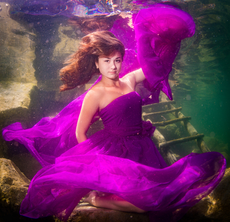 Young graceful woman in a dress posing near the stairs in the lakeの写真素材