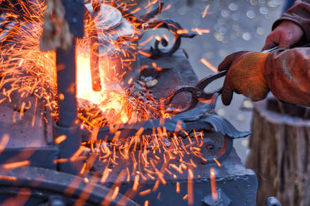 The smith is working on the horseshoe on a small forge furnace. Visible sparks in the forge and flying fire. Horseshoe forging at the Russian fair in Moscow.の写真素材