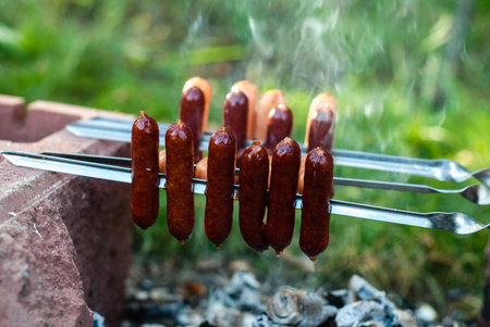 Smoked sausages are fried on a fire (on coals). Meat sausages on skewers. Cooking food while...