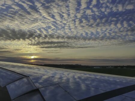 Clouds and blue sky reflecting on airplane wing at sunset.の写真素材