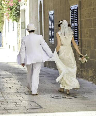 Summer wedding in old medieval city on Malta walking together by the ancient street in a glamorous white wedding dressの写真素材