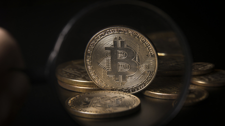 Unrecognizable person holding magnifying glass and looking through it on new virtual money golden bitcoin placed on a black background.の写真素材