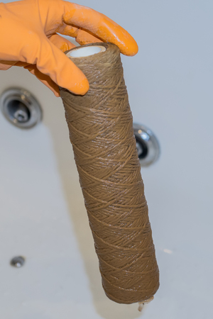 Hand holding dirty water filter cartridge over the bathhub.の写真素材