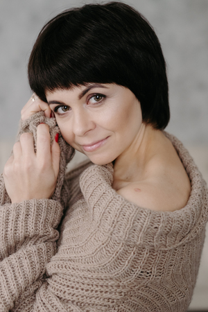 Gorgeous young brunette woman in warm knitted sweater posing on the bedの写真素材