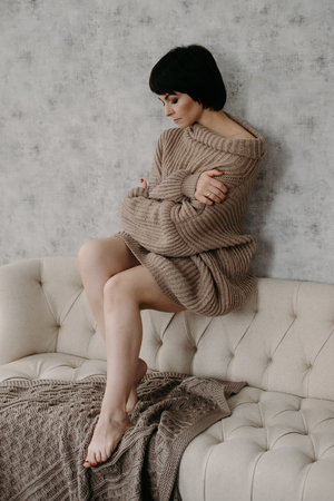 Gorgeous young brunette woman in warm knitted sweater posing on the bedの写真素材