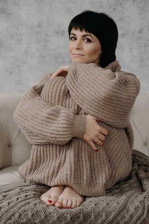Gorgeous young brunette woman in warm knitted sweater posing on the bedの写真素材
