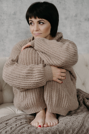 Gorgeous young brunette woman in warm knitted sweater posing on the bedの写真素材