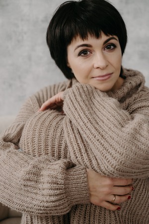 Gorgeous young brunette woman in warm knitted sweater posing on the bedの写真素材