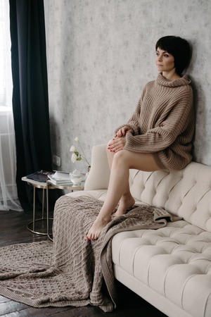 Gorgeous young brunette woman in warm knitted sweater posing on the bedの写真素材