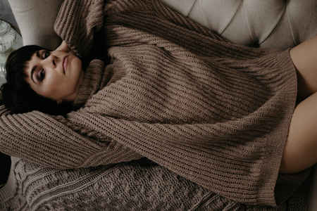 Gorgeous young brunette woman in warm knitted sweater posing on the bedの写真素材