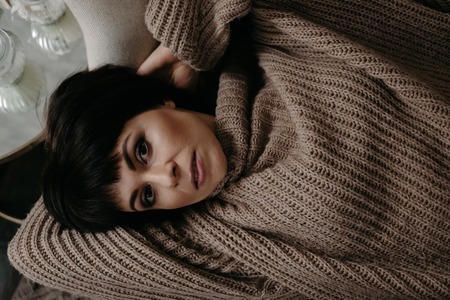 Gorgeous young brunette woman in warm knitted sweater posing on the bedの写真素材