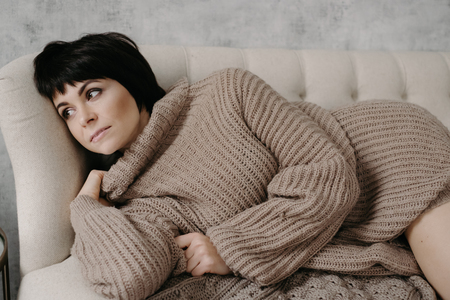 Gorgeous young brunette woman in warm knitted sweater posing on the bedの写真素材