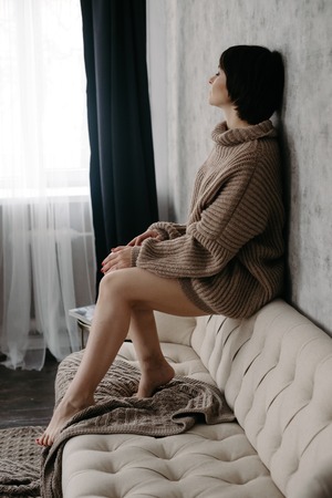 Gorgeous young brunette woman in warm knitted sweater posing on the bedの写真素材