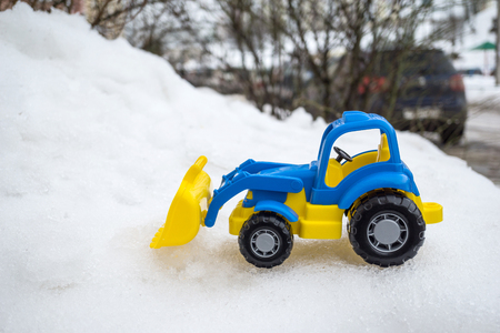 plastic blue and yellow toy tractor with front loader in the snow. concept of utilities and snow removal. road services.の写真素材