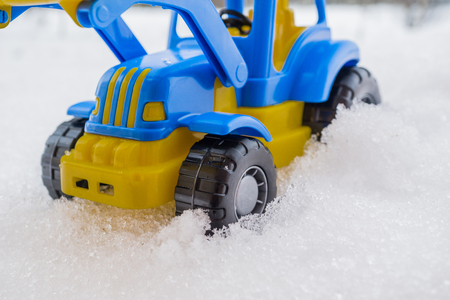 plastic blue and yellow toy tractor with front loader in the snow. concept of utilities and snow removal. road services.の写真素材