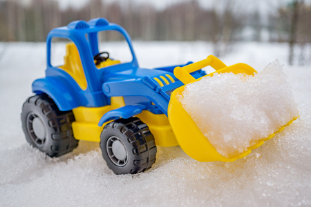 plastic blue and yellow toy tractor with front loader in the snow. concept of utilities and snow removal. road services.の写真素材