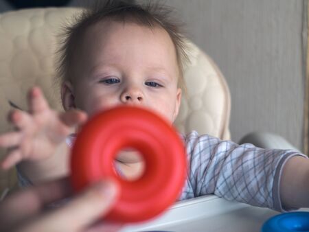 happy toddler baby boy sorting red and blue rings on pyramid sitting in the child chairの写真素材