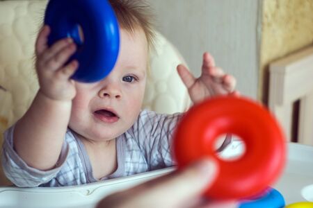 happy toddler baby boy sorting red and blue rings on pyramid sitting in the child chairの写真素材
